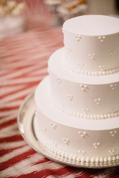 a three tiered white wedding cake sitting on top of a silver platter with red and white checkered tablecloth