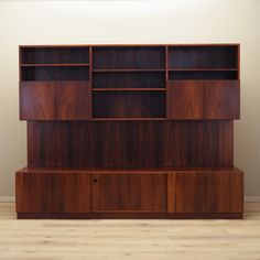 a large wooden shelf with shelves and drawers on the top, in front of a white wall