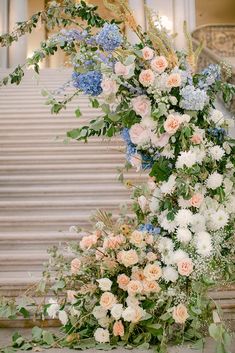 an arrangement of flowers and greenery in front of a stair case at a wedding