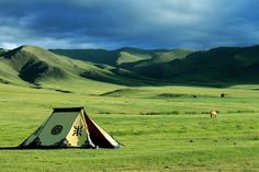 a tent in the middle of a field with mountains in the background that says go to mongolia