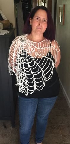 a woman standing in front of a mirror wearing blue jeans and a black top with white lace on it