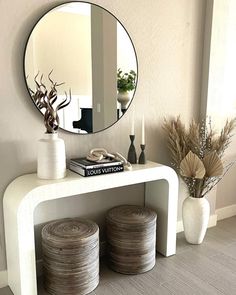 a white table with two vases and a mirror on the wall above it, along with stacks of books