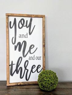 a wooden sign with the words you and me and our three on it next to a green plant