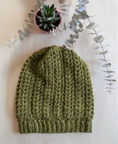 a green knitted hat sitting on top of a table next to a potted plant