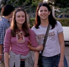 two young women standing next to each other on a brick walkway with trees in the background