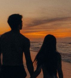 two people walking on the beach at sunset