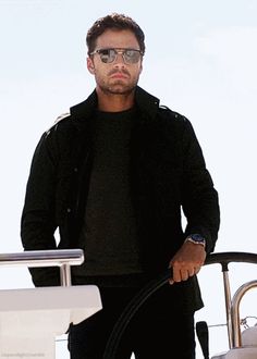 a man standing on top of a boat next to a steering wheel with a hose in his hand