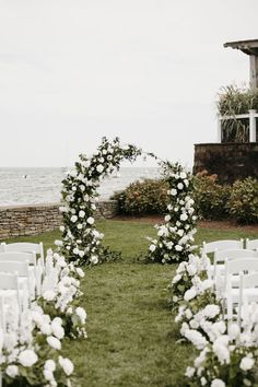 an outdoor ceremony set up with white flowers and greenery on the grass by the water