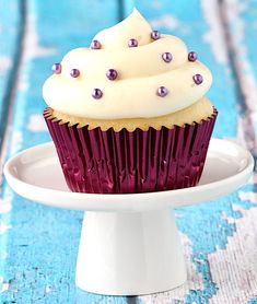 a cupcake with white frosting and purple sprinkles on a plate