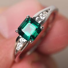 an emerald and diamond ring on someone's finger