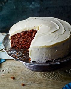 a carrot cake with white frosting is on a plate and has one slice cut out