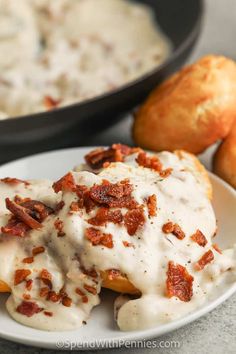 a white plate topped with meat covered in gravy next to some bread rolls