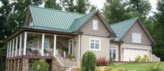 a large house with green roofing and white trim on the front porch, surrounded by lush greenery