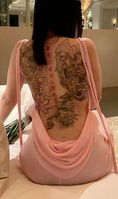 a woman sitting on top of a bed with tattoos on her back and arms behind her