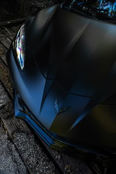 the front end of a black sports car parked on top of a wooden platform next to trees