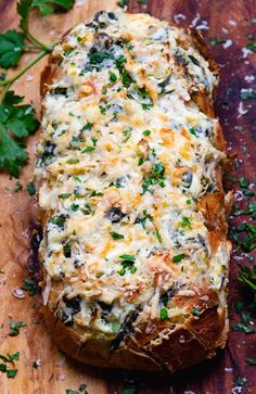 a loaf of bread topped with cheese and vegetables on a wooden cutting board next to parsley