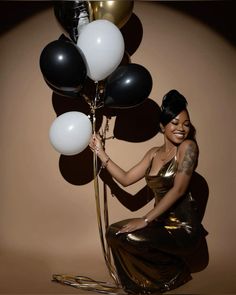 a woman in a gold dress is holding some black and white balloons while sitting on the floor