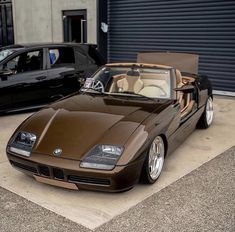 two cars parked next to each other in front of a garage door and one is brown