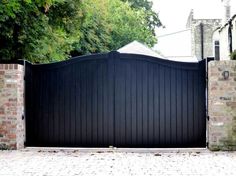 a black gate with brick walls and trees in the background