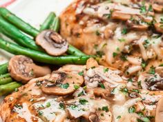 two pieces of chicken covered in mushrooms and green beans on a plate with asparagus