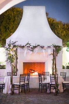 an outdoor fireplace with tables and chairs set up for a formal function at night time