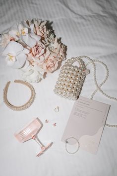 the contents of a bridal gown laid out on a bed with flowers and jewelry