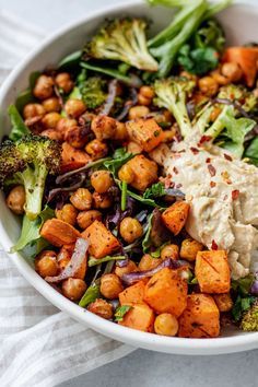 a white bowl filled with vegetables and chickpeas on top of a table cloth