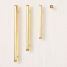 two brass handles and one gold handle on a white surface