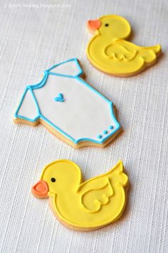 three decorated cookies sitting on top of a white cloth covered tablecloth with yellow rubber ducks