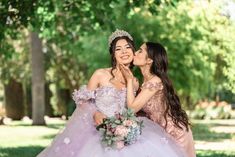 two women in dresses are kissing and posing for the camera with trees in the background