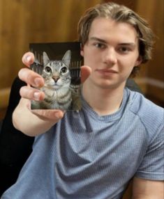 a young man holding up a small card with a cat on it