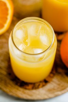 a glass filled with orange juice next to sliced oranges on a wooden platter