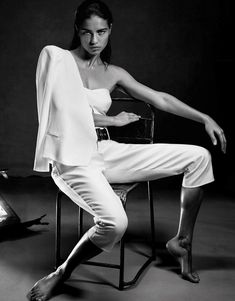 a woman sitting on top of a chair wearing white pants and a blazer jacket