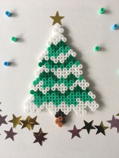 a christmas tree made out of perler beads on a white surface with stars around it