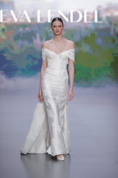 a model walks down the runway in a white gown with an off - shoulder design