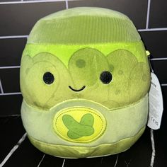 a green stuffed animal sitting on top of a tiled floor next to a black tile wall