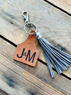 a leather keychain with the initials and tassels on it sitting on a wooden surface