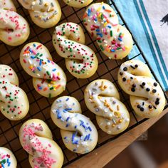 many donuts with sprinkles are on a cooling rack and ready to be eaten