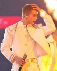 a male in a white suit is holding his hand up to his head while standing on stage