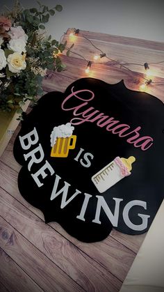 a wooden sign that says beer is brewing on the side of a table with flowers and lights in the background