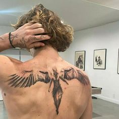 a man with tattoos on his back is holding his hand to his head and looking at himself in the mirror