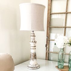 a white table with a lamp and vases on it next to an old window