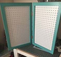 an open green and white cabinet sitting on top of a wooden table with holes in it