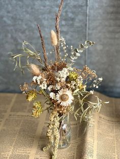 a vase filled with lots of flowers sitting on top of a table next to a newspaper