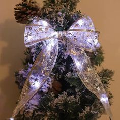 a lighted bow on top of a christmas tree with snowflakes and pine cones