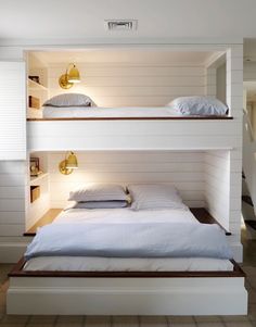 two bunk beds with white sheets and pillows in a room that has wood flooring