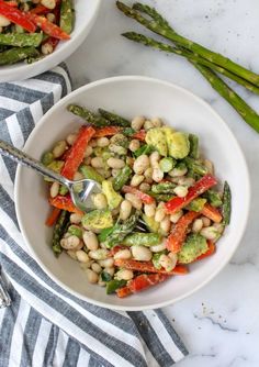 two white bowls filled with vegetables on top of a table