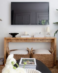 a flat screen tv mounted on the wall above two wicker baskets and a coffee table