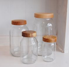 three glass jars with wooden lids on a white surface