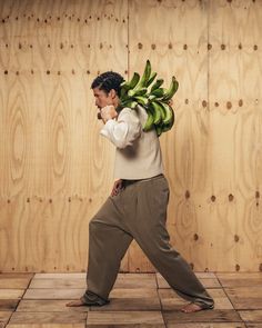 a man with a bunch of bananas on his back walking across a tile floor in front of wooden walls